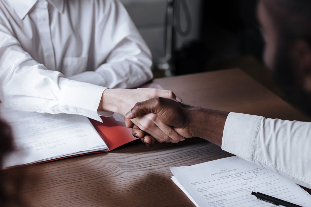 A handshake over a stack of documents at a desk.